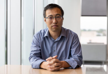 A photo of a man sitting at a desk indoors.